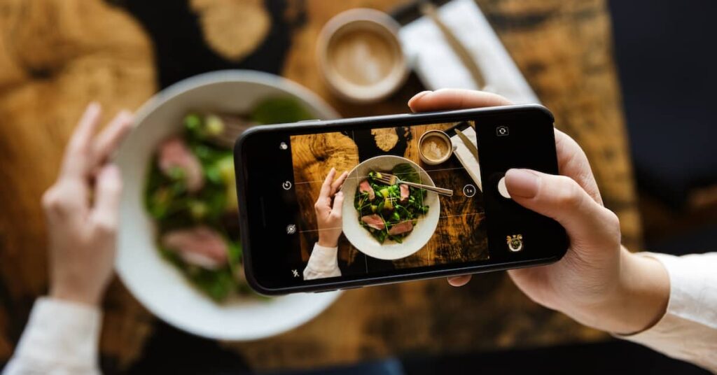 Female restaurant customer taking a picture of her meal with a smartphone to post on social media | Twelve Three Media